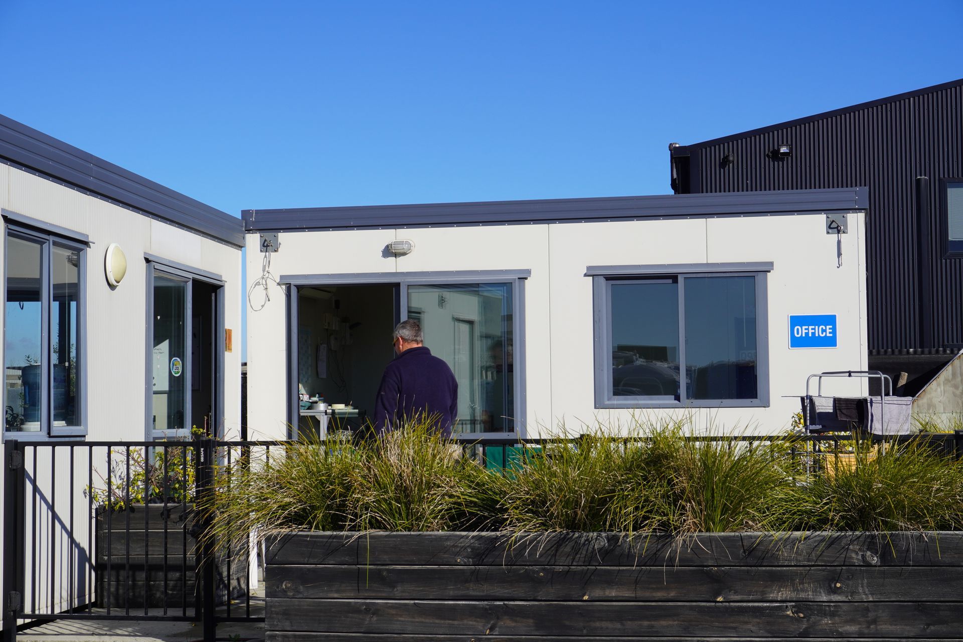 Smith's Loos Head Office, a man standing inside a white modular building with windows. Exterior view of the building on a sunny day.