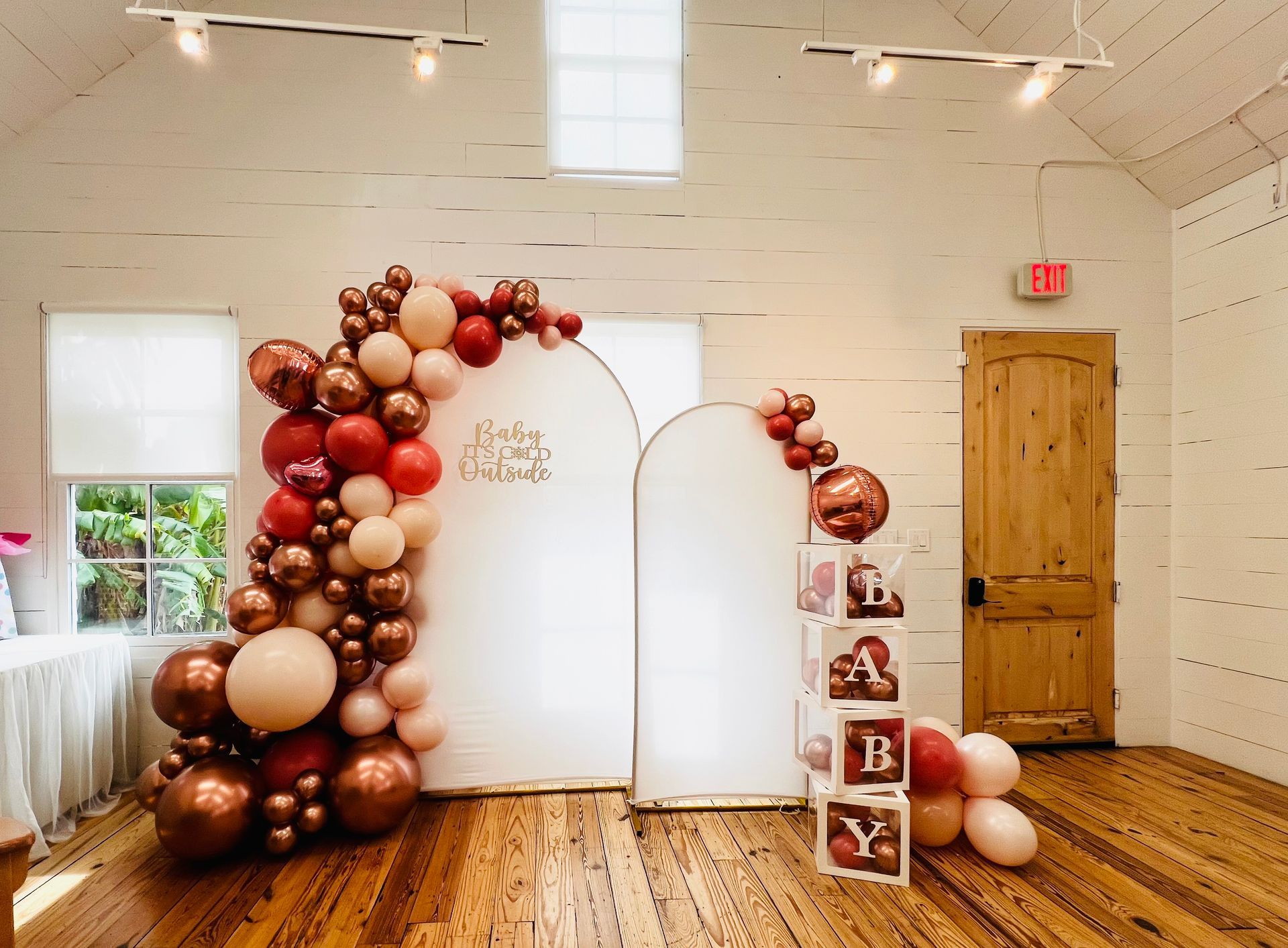 White ceremony backdrop with burgundy and blush balloon arch and “BABY” blocks in a bright room