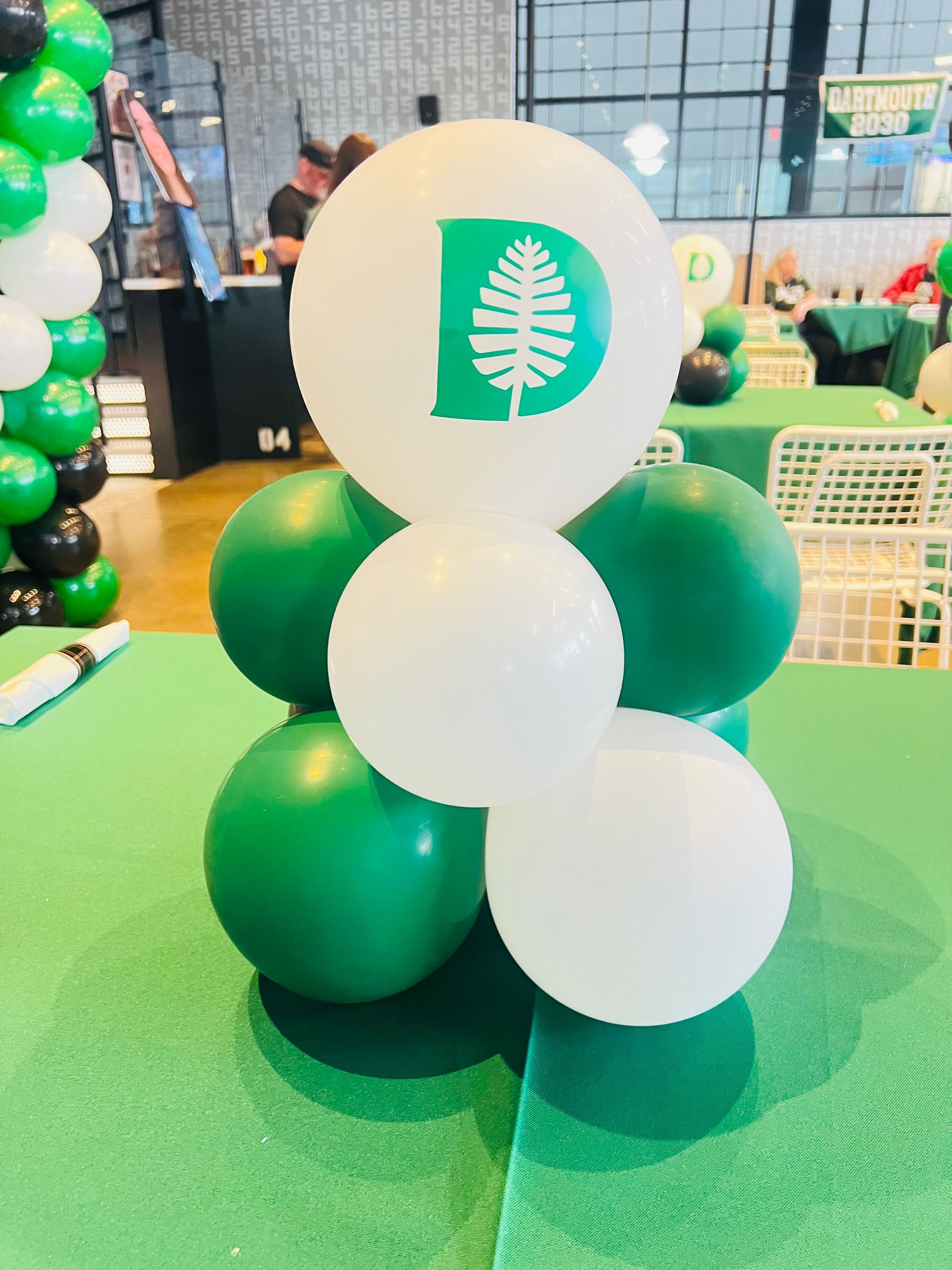 Green and white balloon sculpture with a circular logo on top, displayed indoors on a green floor.