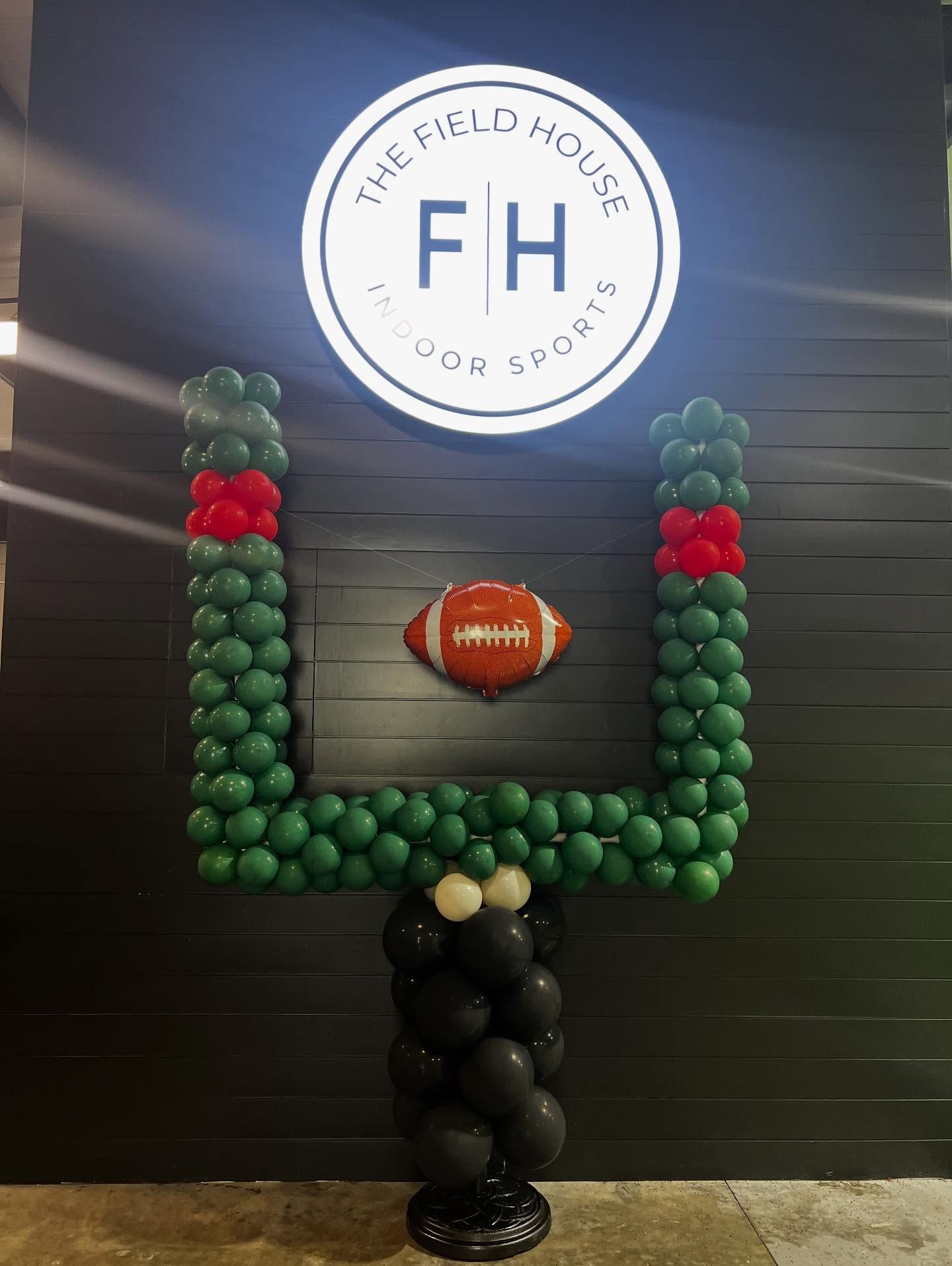Football balloon sculpture in green, red, black, and gold under a circular FH sign at The Field House