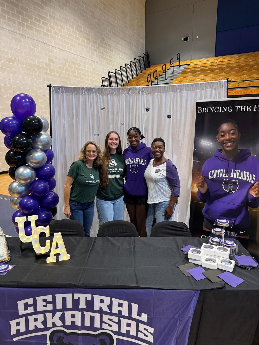 Central Arkansas booth with four people posing behind a table under gray drapes and purple balloons
