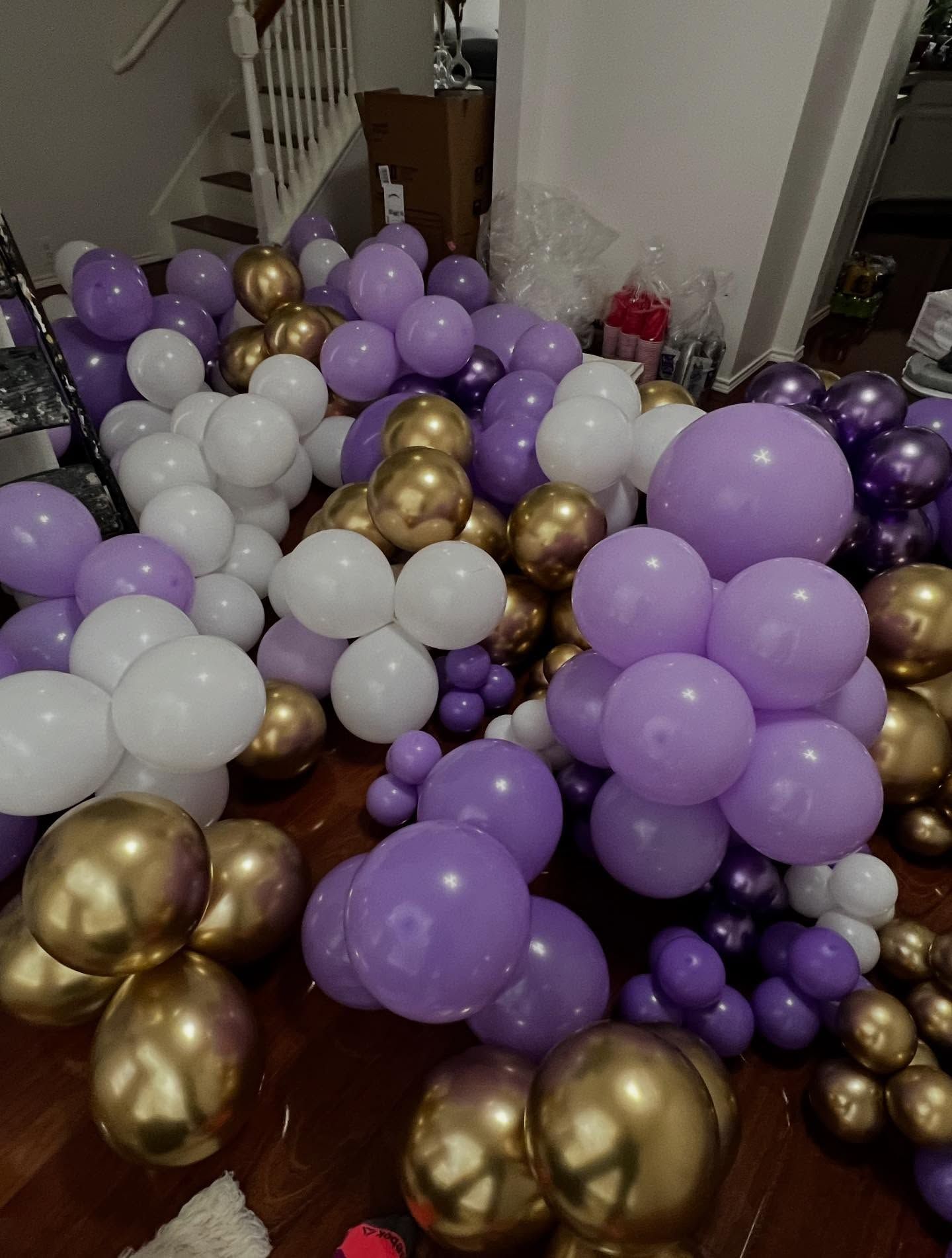 Clusters of purple, white, and gold balloons scattered across a room floor and doorway