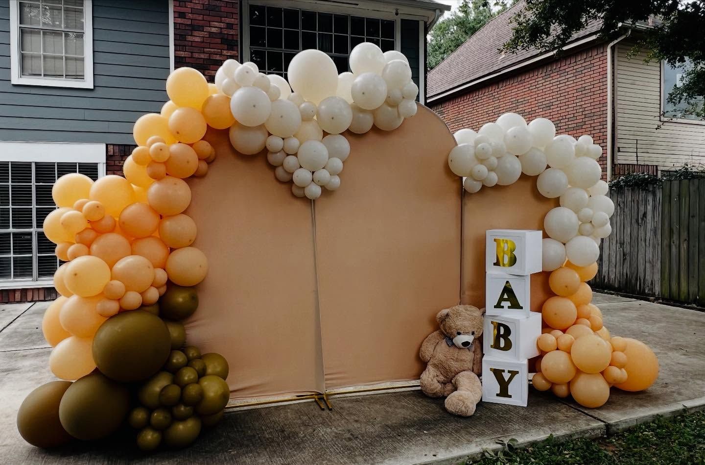 Balloon-decorated baby shower backdrop with white and gold balloons and a “BABY” sign outdoors