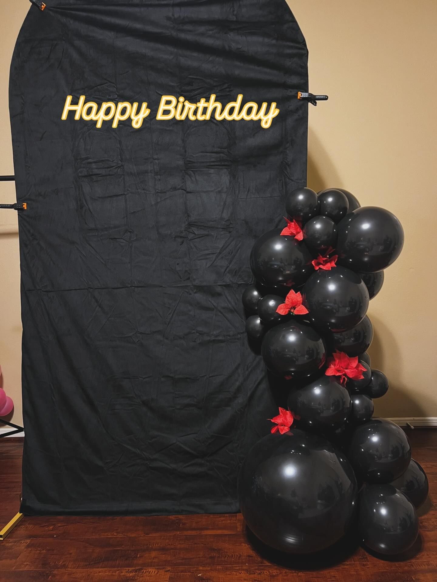 Happy Birthday banner on black backdrop with black and red balloon arrangement at right