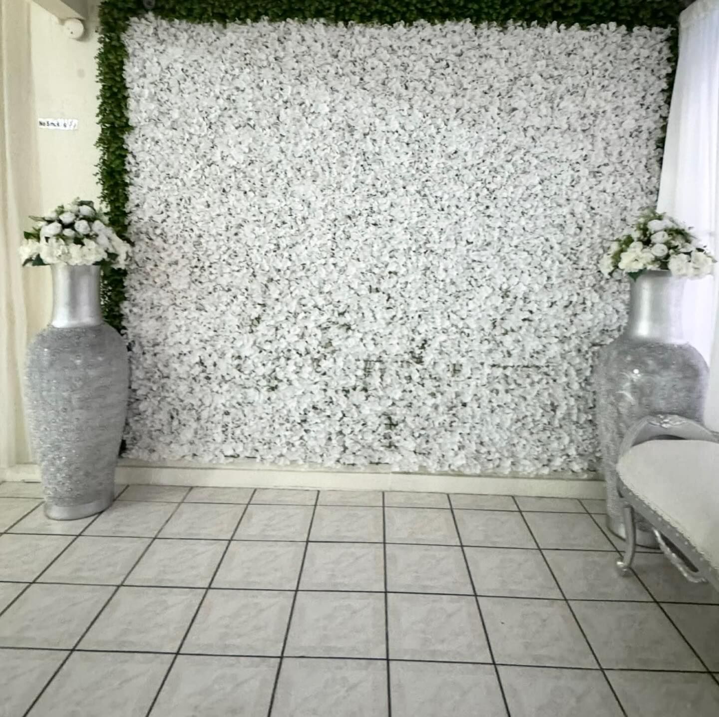 White floral backdrop with silver vases and arrangements beside a tiled floor