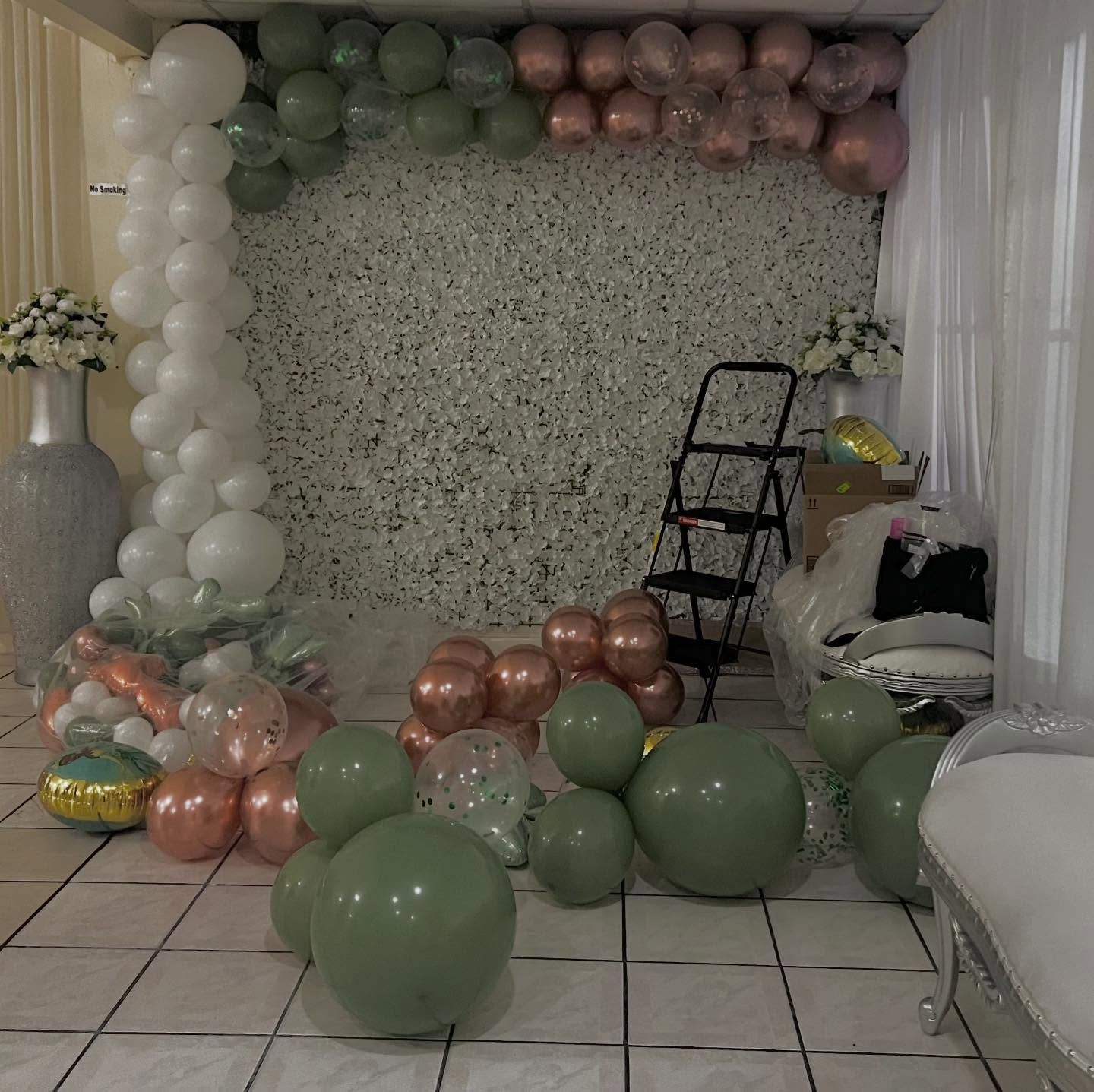Pastel balloon garland and scattered balloons in a decorated room, with a ladder and curtains on the right.
