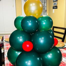 Stack of green and gold balloons on a dining table, with a small red balloon near the front