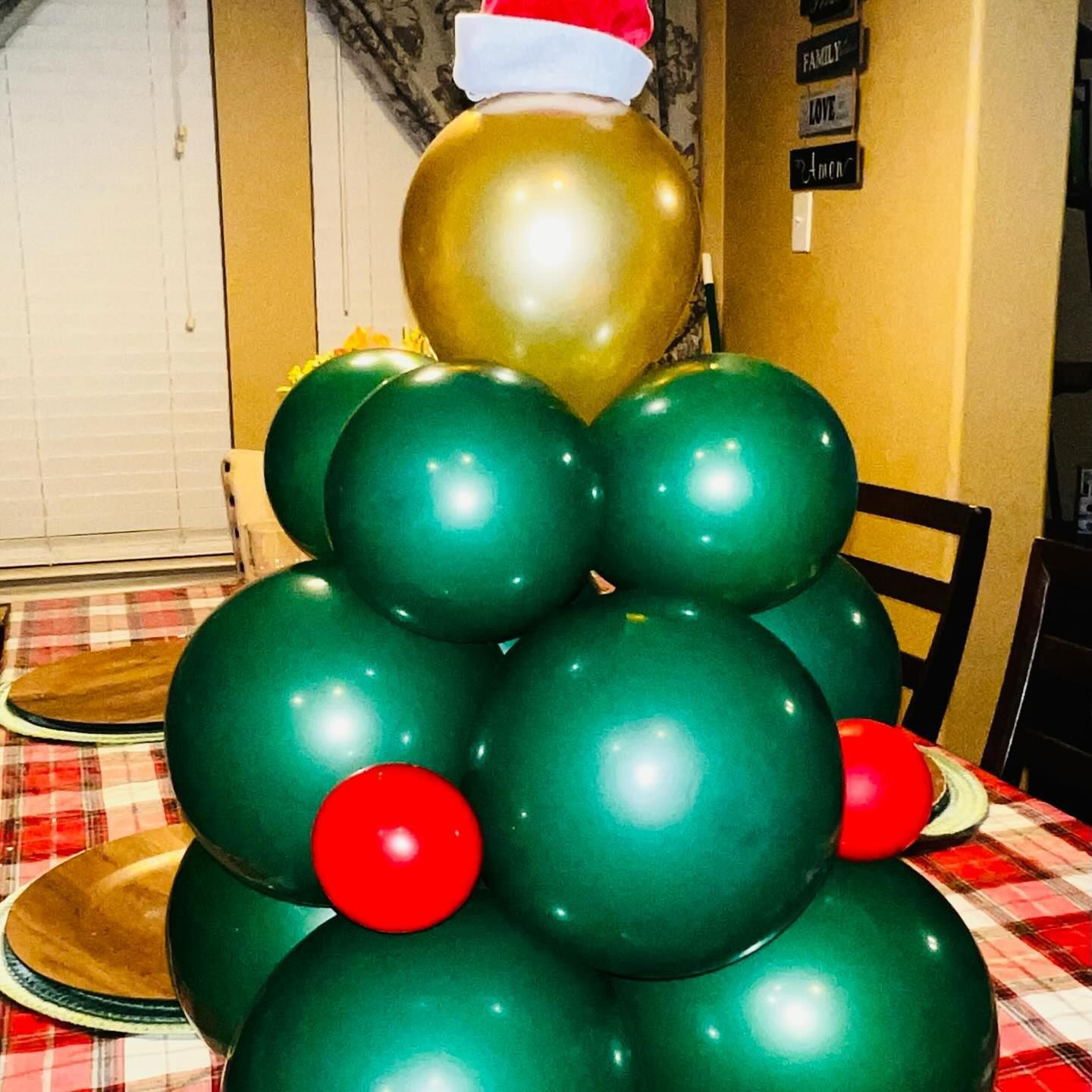 Balloon Christmas tree centerpiece with green and gold balloons, red accents, and a Santa hat