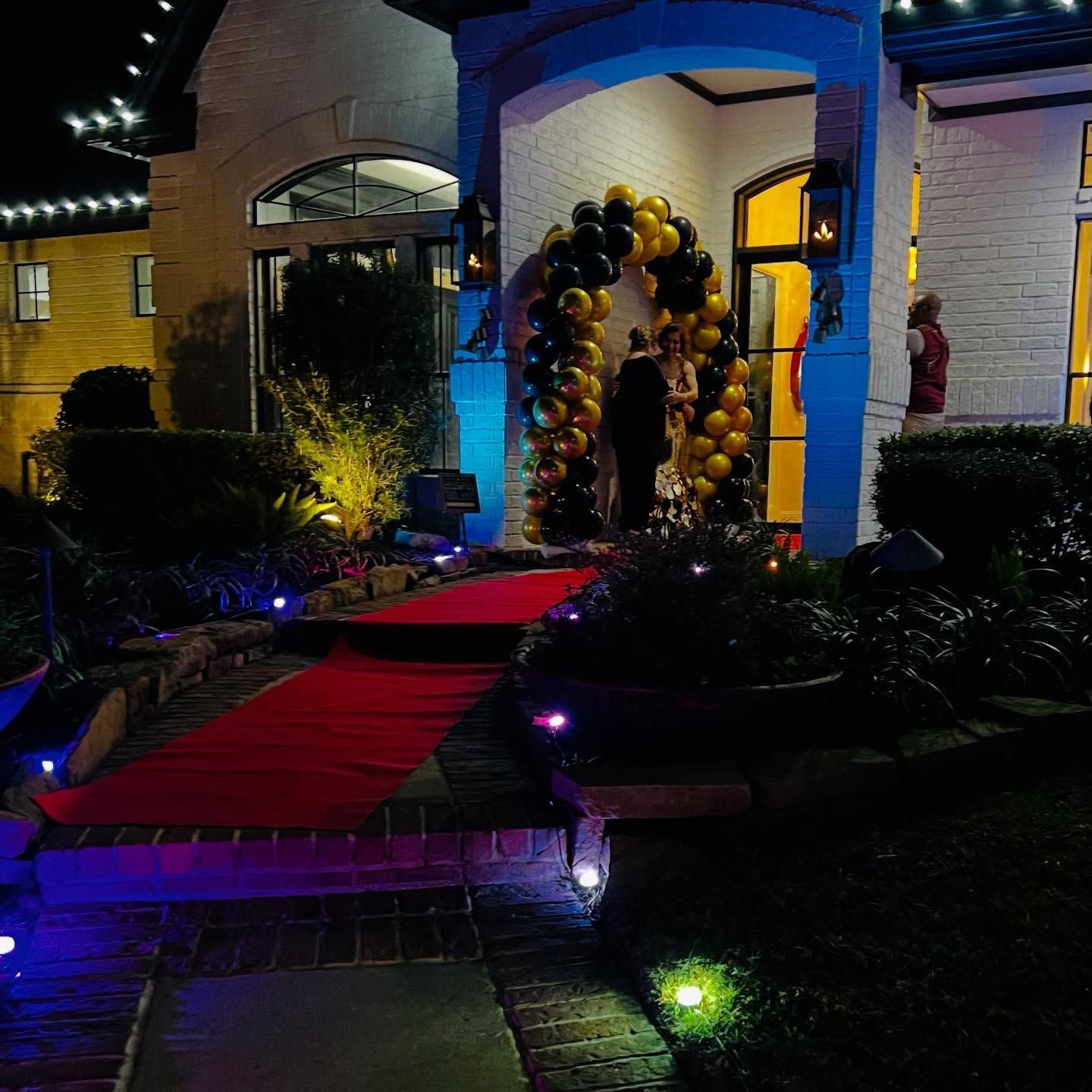 Red-carpet entrance with black and gold balloon arch outside a lit building at night