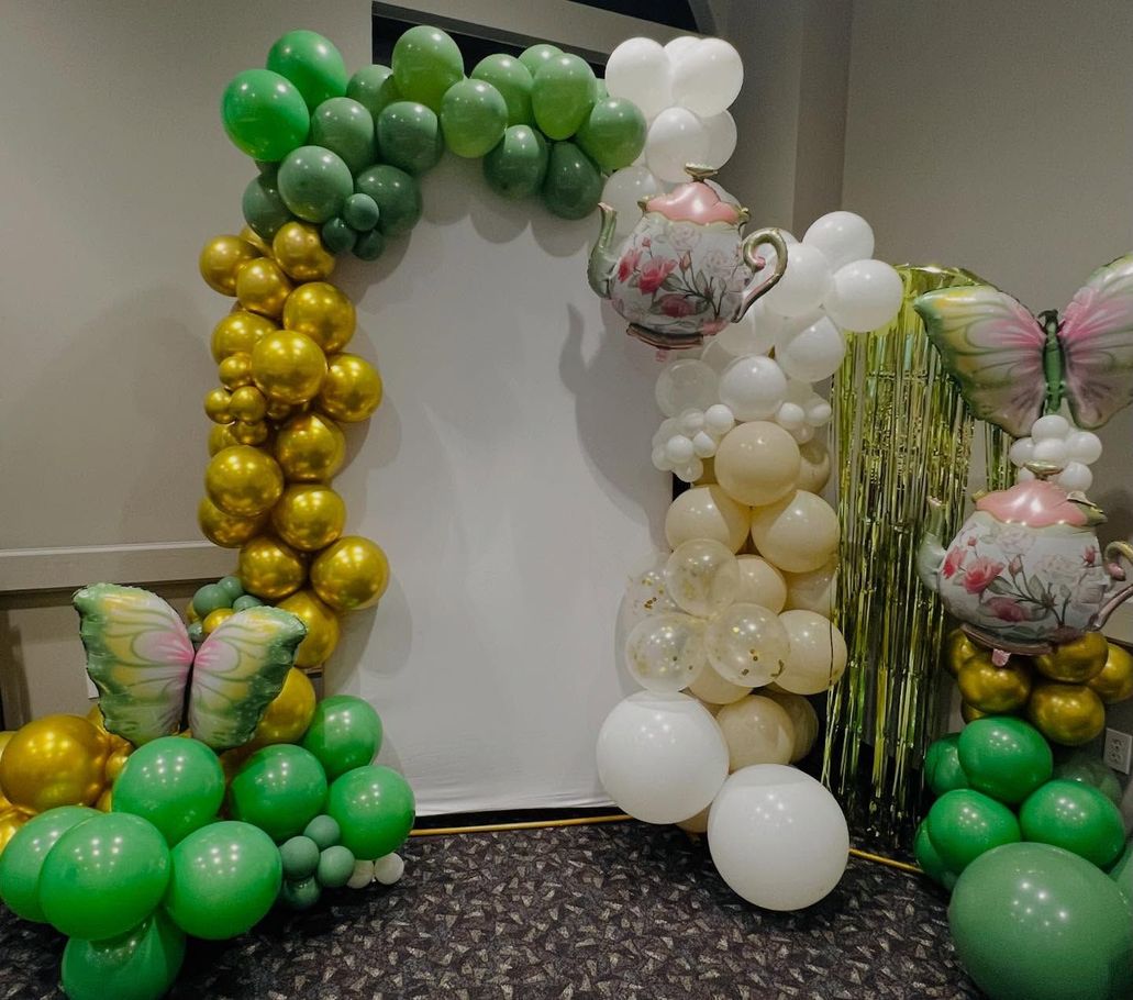 Balloon arch in green, gold, white, and pink decorating a hallway wall