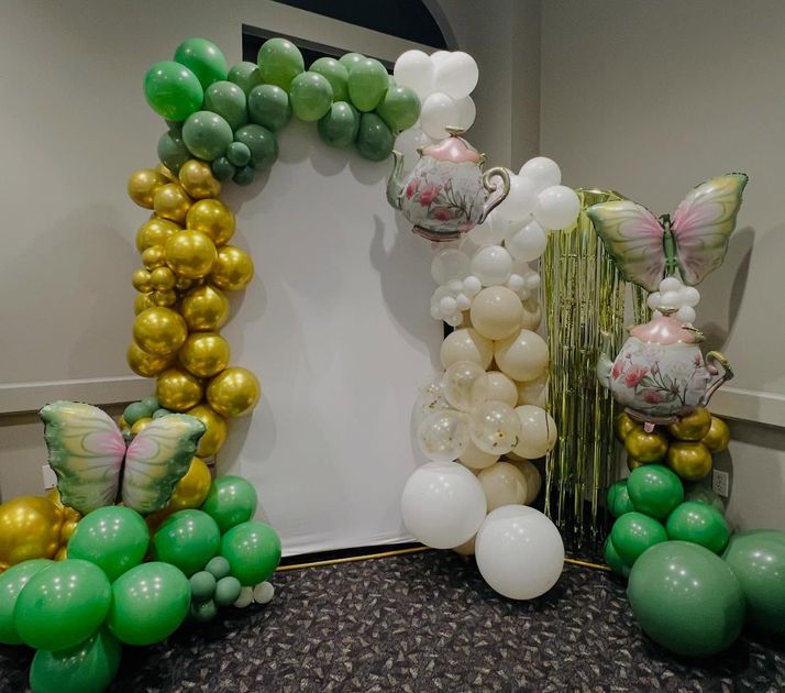 Balloon arch with green, gold, and white balloons on a carpeted event backdrop