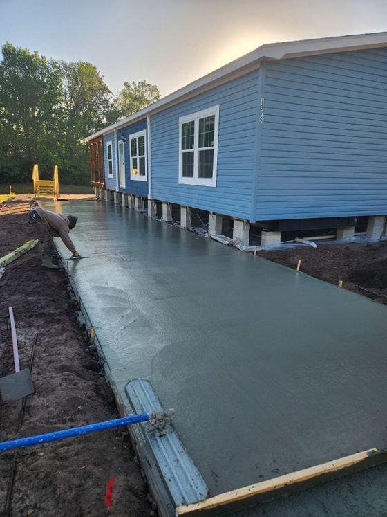 A man is spreading concrete on a sidewalk in front of a mobile home.