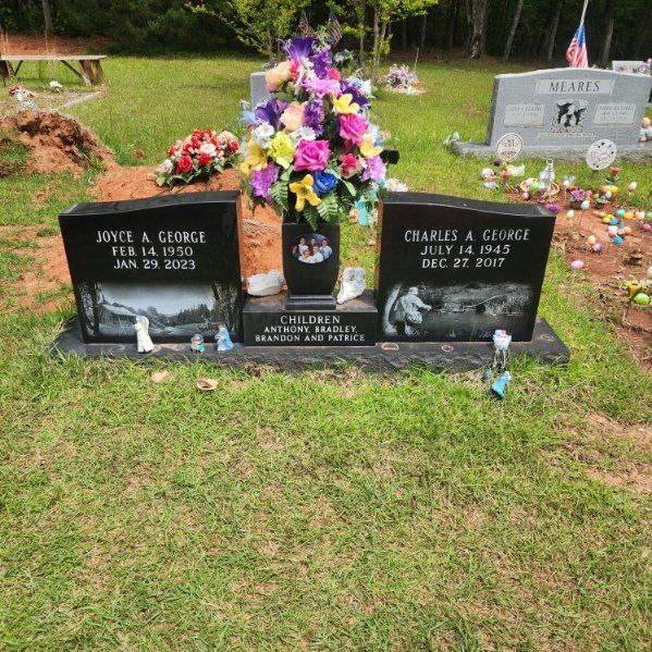 A double gravestone with flowers. Names are JONCE A. GEORGE and CHARLES A. GEORGE with dates. Set in a grassy cemetery.