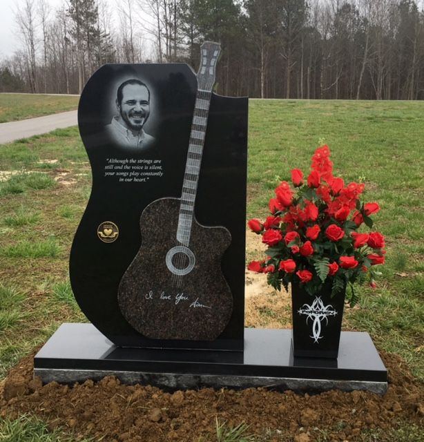 Black granite headstone with guitar, photo, inscription, and red roses.