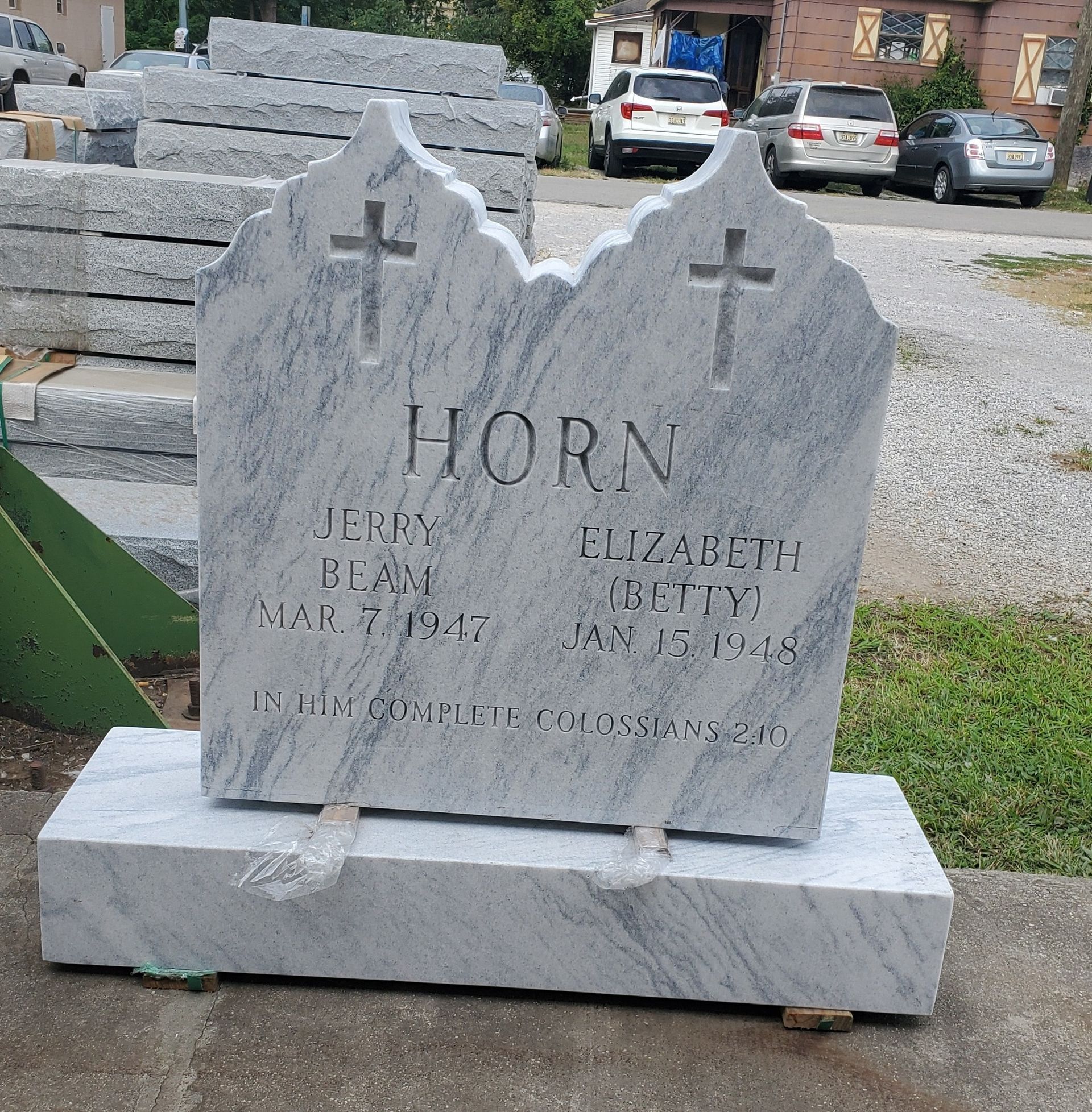 A white marble headstone with etched names, crosses, and dates; set in an outdoor yard.