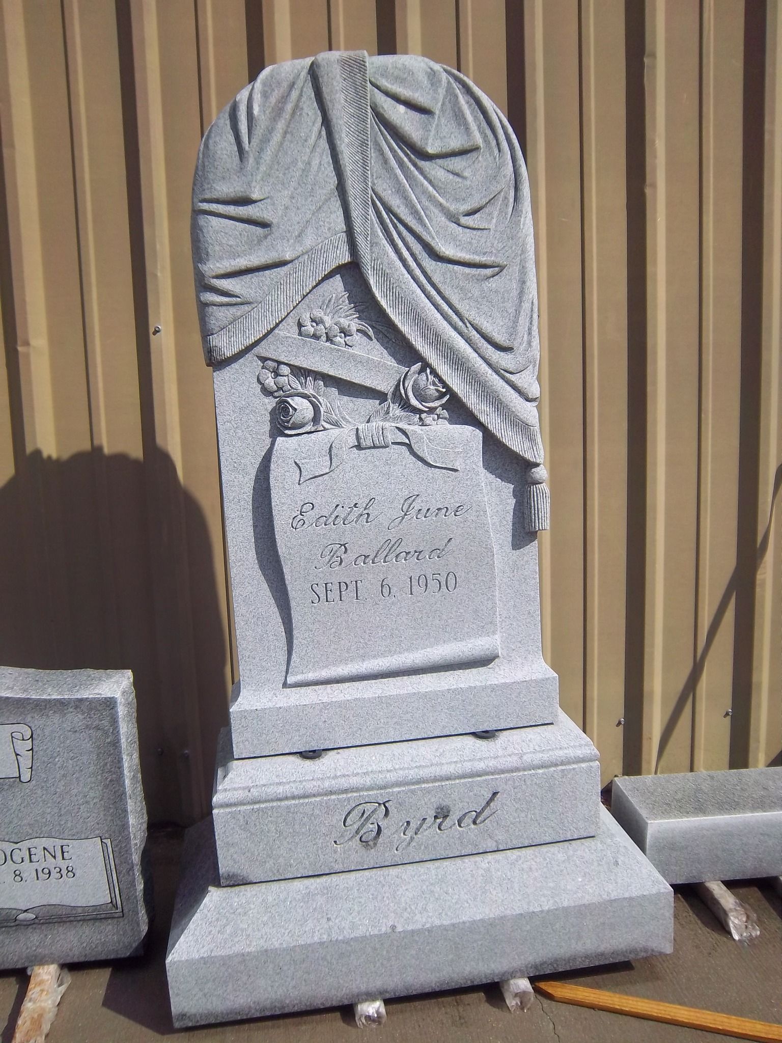 Gray granite headstone with draped fabric design and inscription.