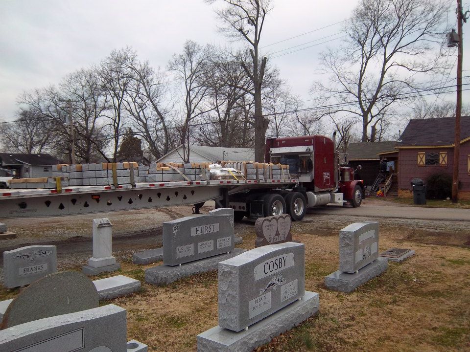 Semi-truck parked next to a cemetery, loaded with construction materials. Gray headstones in foreground.