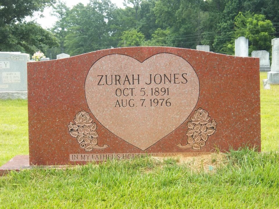 Black granite headstone with name, dates, and etched scene of barn and deer. Two black vases flank it.