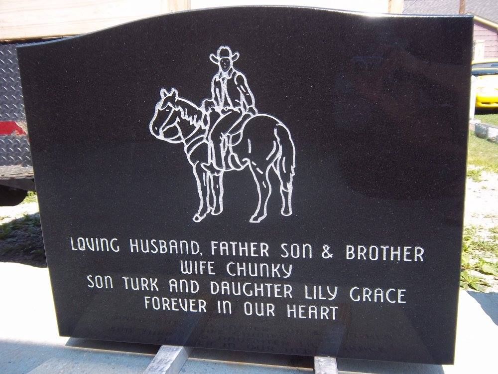 Black granite tombstone with a rider on a horse etched in white, inscribed with a tribute to a loved one.