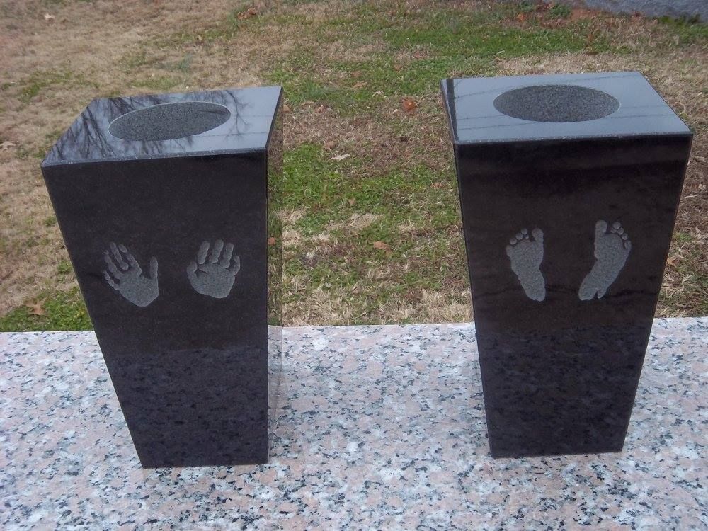 Two dark granite pedestals with hand and foot impressions, each with a circular opening at the top.