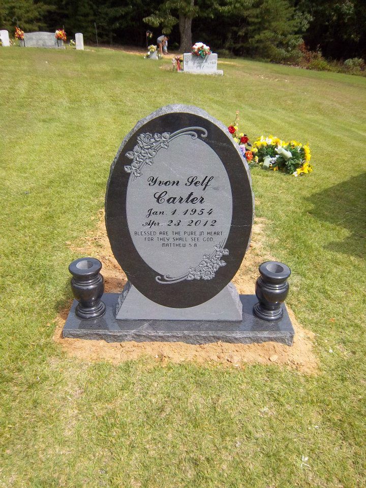 Headstone in a cemetery with a dark oval shape and floral accents. Two vases sit in front.