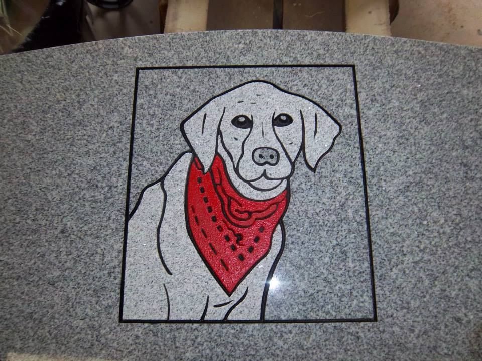 Dog portrait etched in gray stone, wearing a red bandana, within a black bordered square.