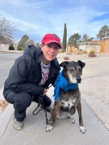 Colleen Kelley, the owner of Beck 'n Call Pet Services in Albuquerque New Mexico standing outside with an old black dog