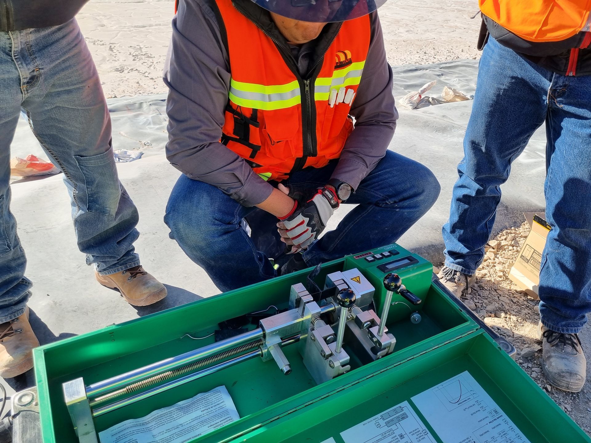Una persona usa una máquina de pruebas al aire libre. Lleva chaleco salvavidas y vaqueros, y hay otras dos personas cerca.