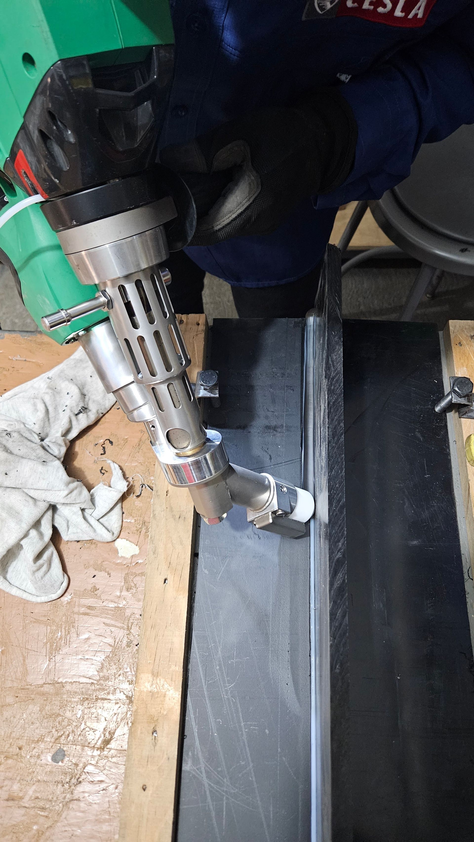 Persona que utiliza una herramienta de soldadura de plástico portátil sobre una superficie oscura, en el interior.