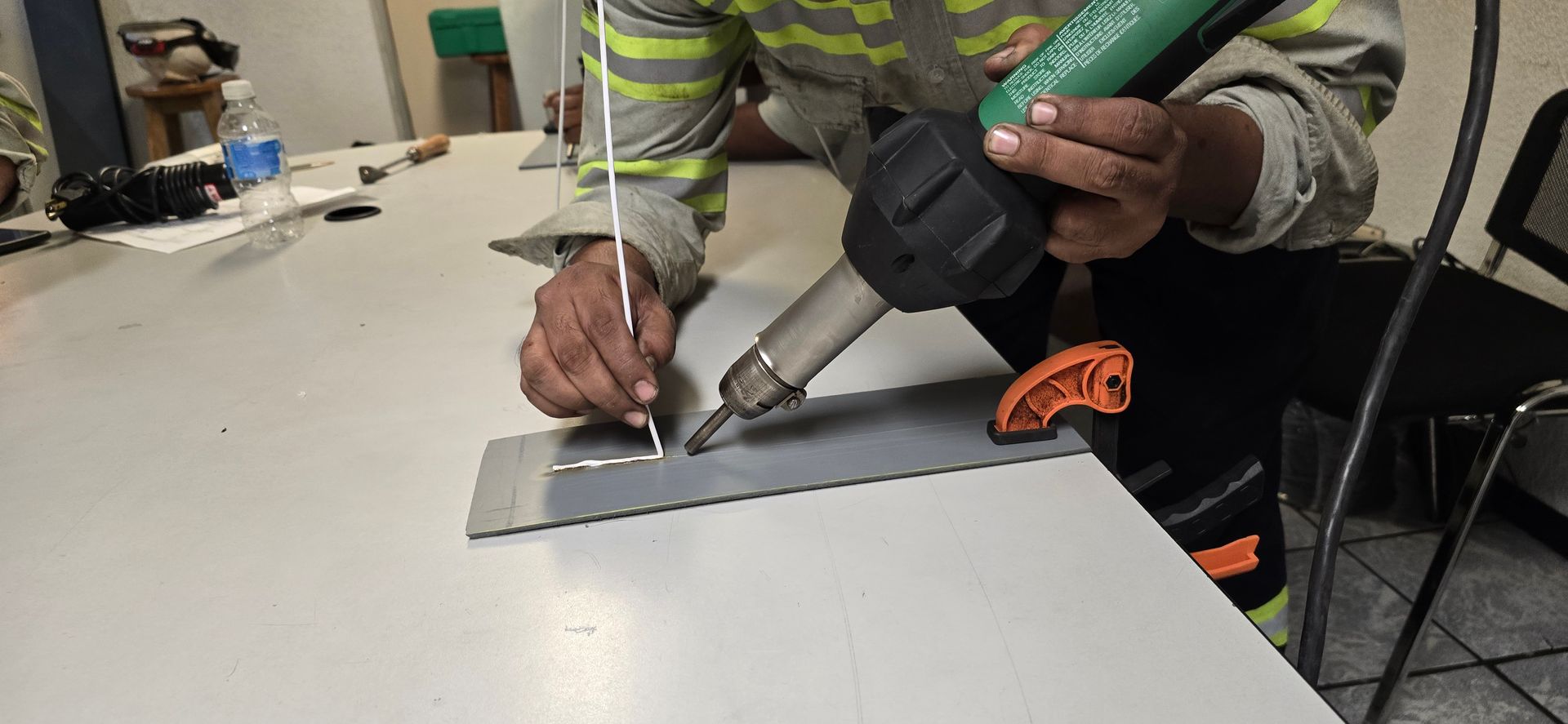 Persona que utiliza una pistola de calor para soldar una lámina de metal sobre una mesa.