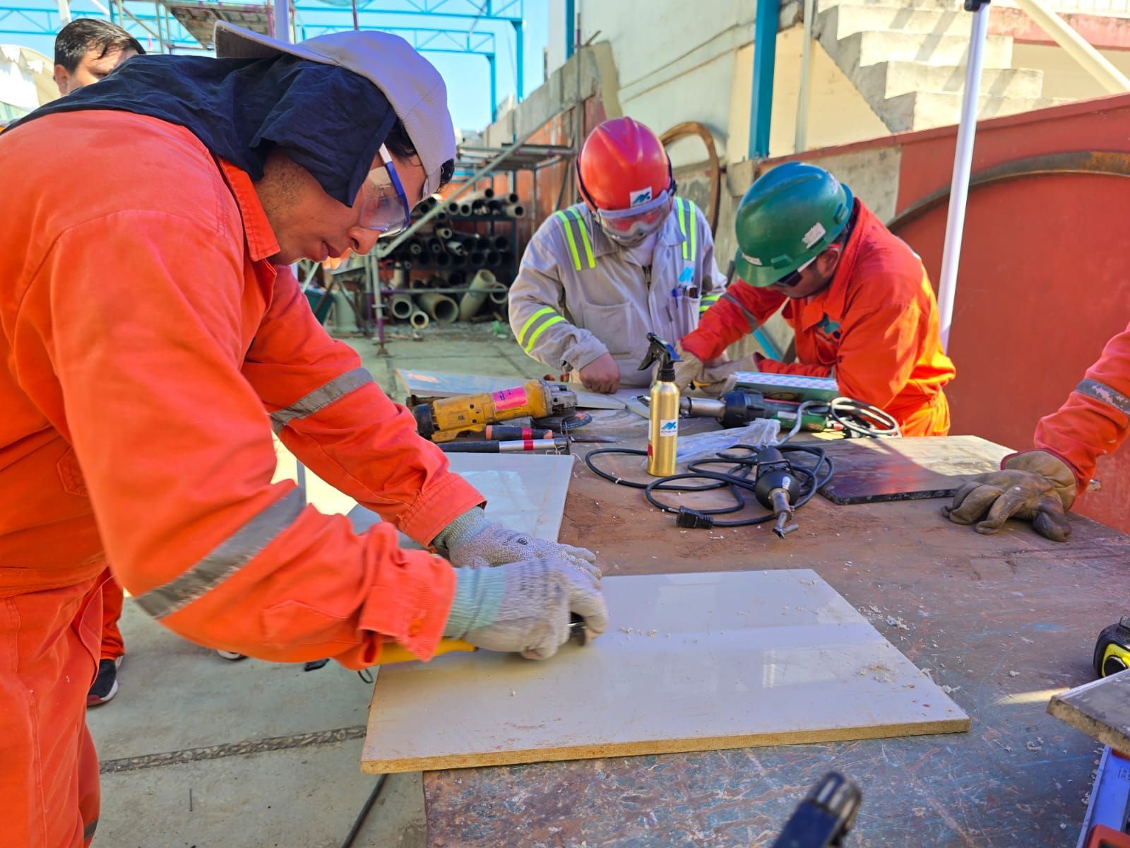 Trabajadores con overoles de color naranja y cascos cortando madera al aire libre.