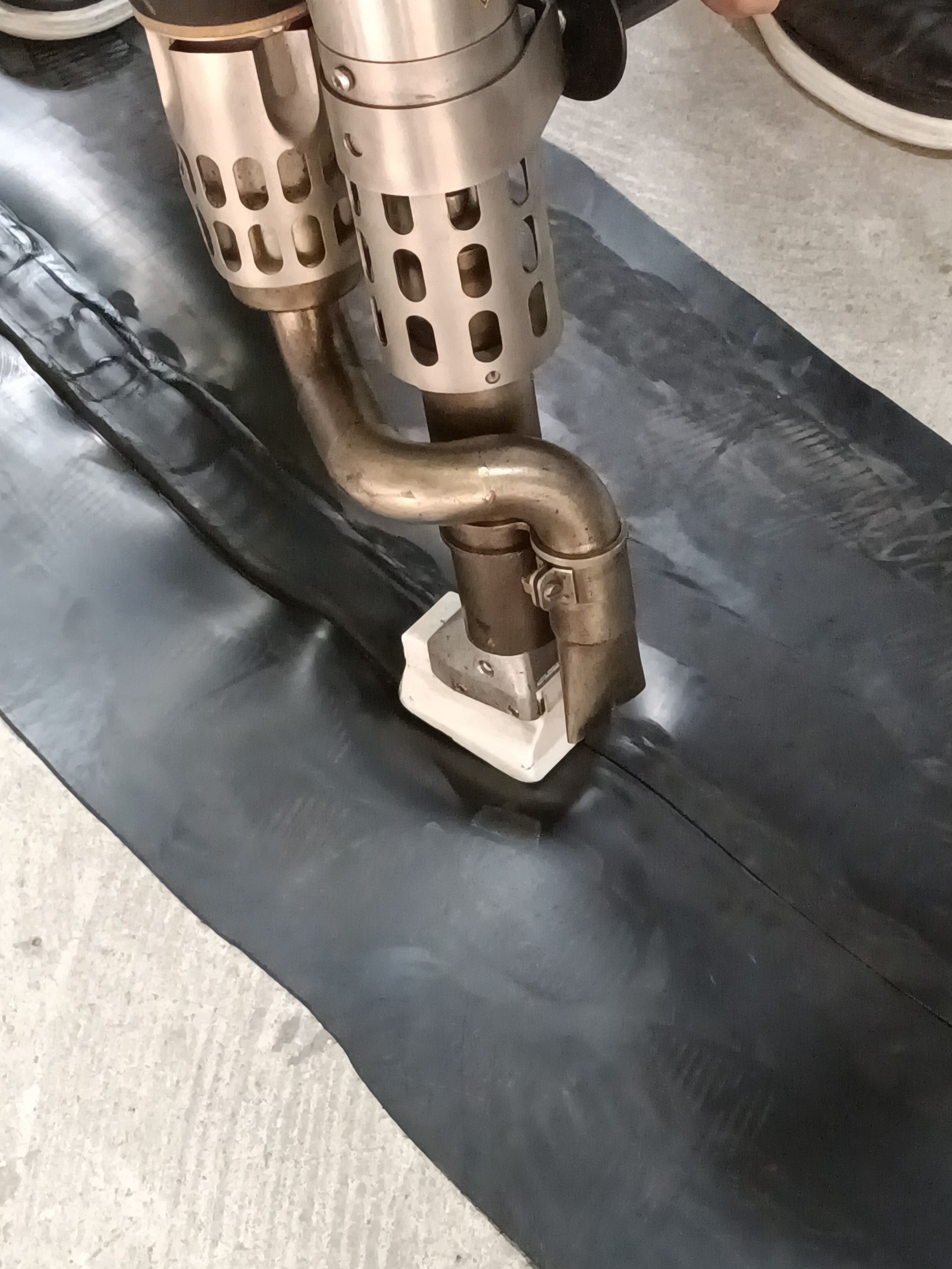 Una persona suelda una costura en una membrana de caucho negra con una herramienta de soldadura de aire caliente.