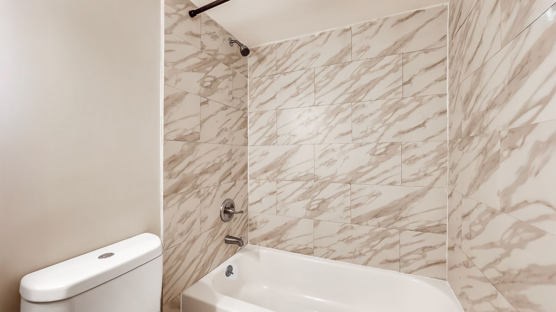 Modern bathroom with marble tile shower and white bathtub next to a toilet