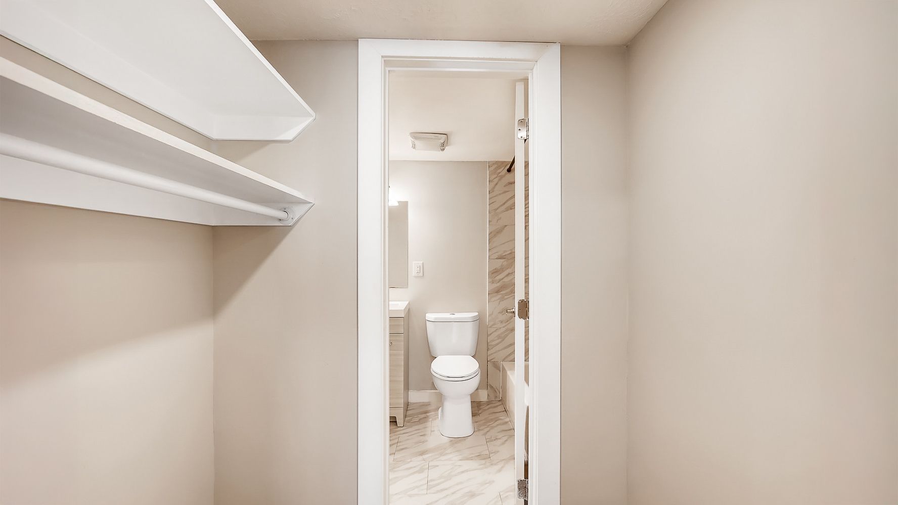 Narrow beige hallway leading to a small bathroom with a white toilet and tiled floor