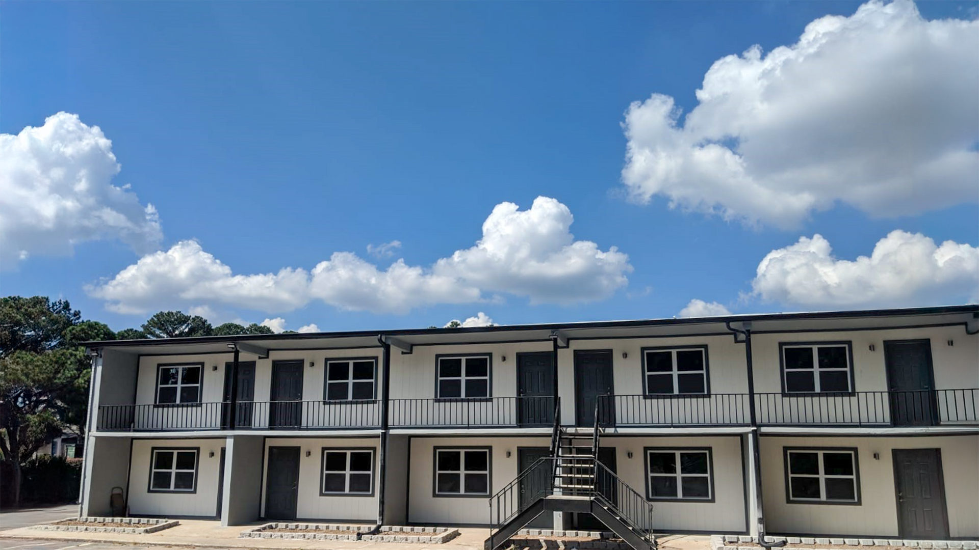 Two-story white apartment building under a bright blue sky with large clouds