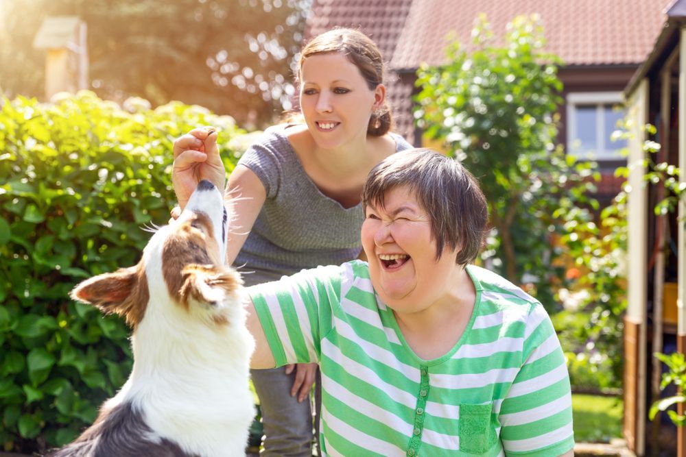 Woman With Down Syndrome Laughs as Another Woman Gives a Treat — Canine Training School in Trinity Park, QLD