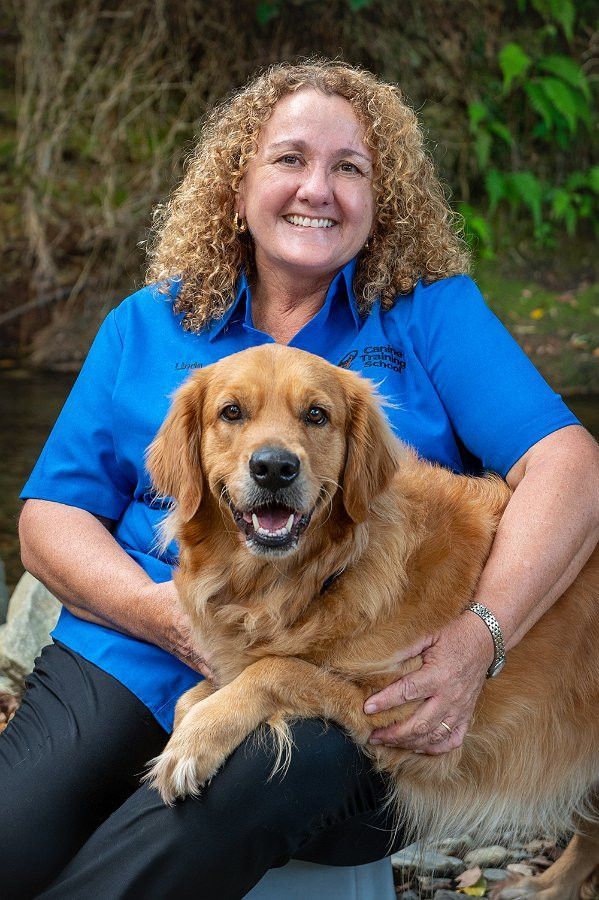 Woman in blue shirt seated with a golden retriever dog outdoors; both smiling.— Canine Training School in Trinity Park, QLD