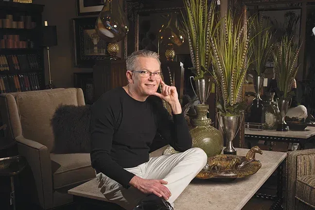 Man seated on a table in a home decor shop, talking on the phone. Neutral setting, decor in background.