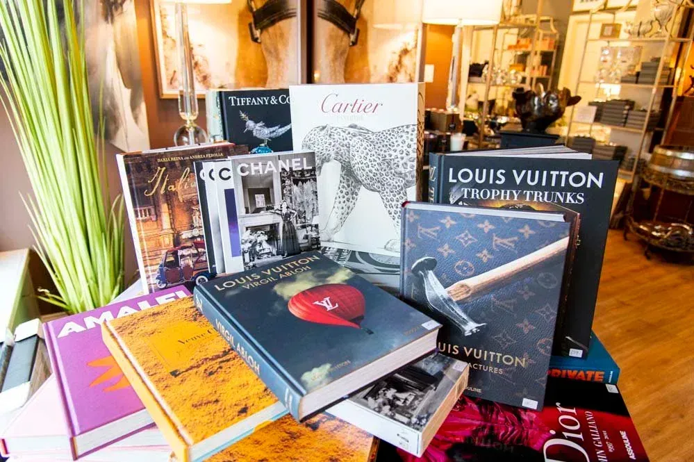 Books by high-end fashion brands like Louis Vuitton, Chanel, and Cartier displayed on a table.