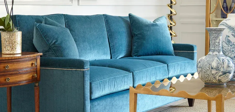 Blue velvet sofa with pillows, wooden side table with orchid, gold-trimmed coffee table, and blue and white vases.