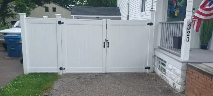 White double gate in front of a house, with black hinges and a lock. The house has a porch with a US flag.