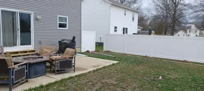 Backyard with patio furniture, gray siding, white fence, and grassy lawn.