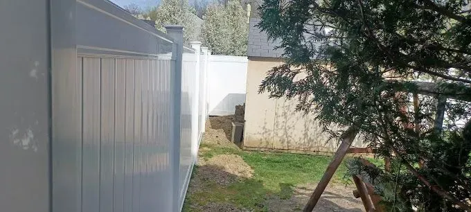 White fence alongside a backyard with grass, a building, and a tree.