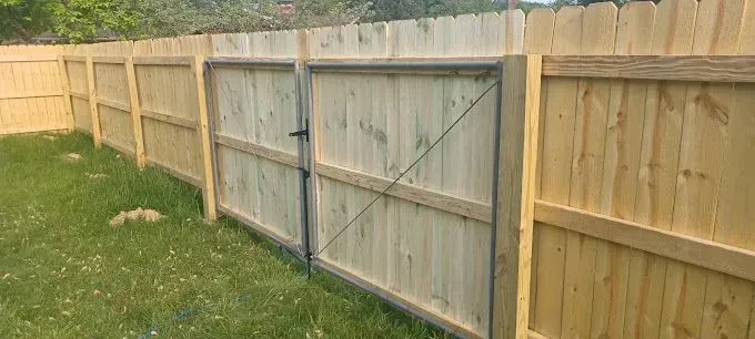 A wooden fence with a gate in a grassy yard.