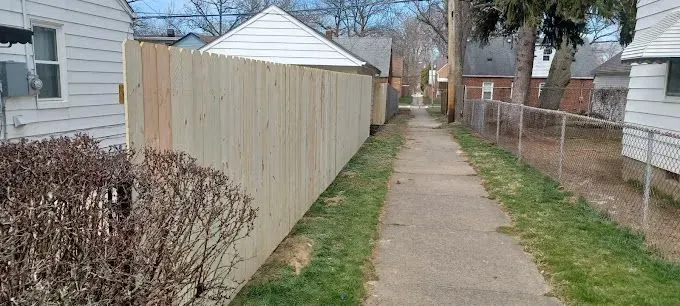 A narrow sidewalk between houses with a wooden fence on one side and a chain-link fence on the other.