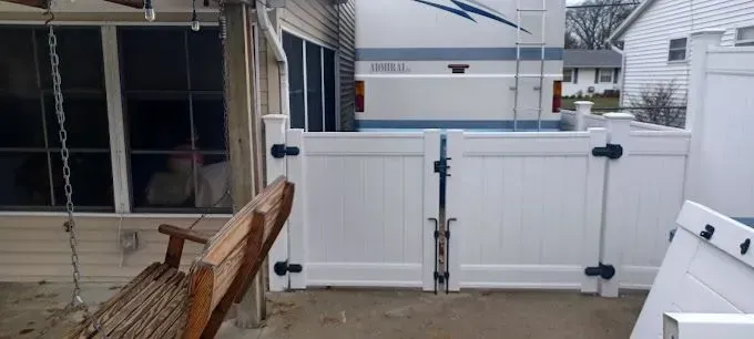 White fence with closed gate near an RV. A wooden bench swing is in the foreground.