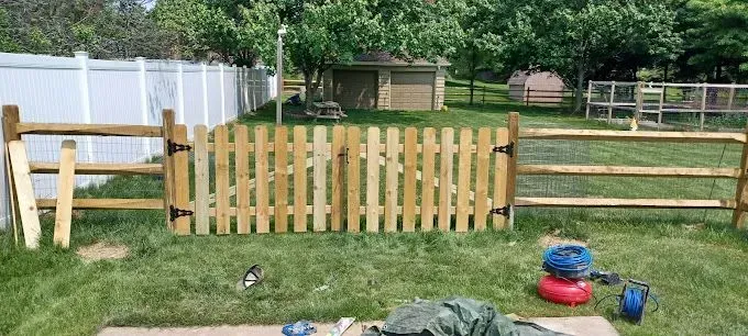Wooden gate in a backyard with a white fence, and a wooden fence.