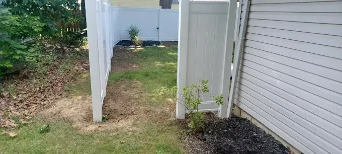 A white fence gate opening to a backyard with grass and a house exterior.