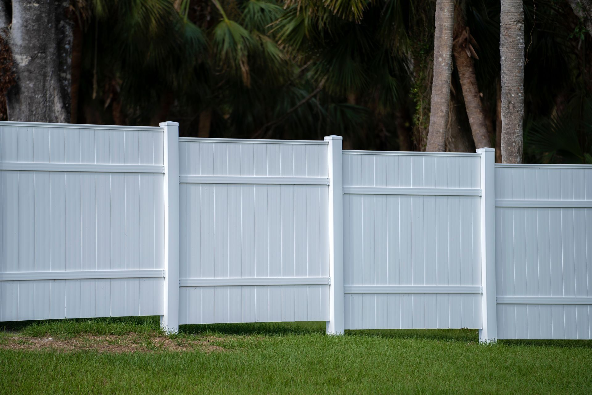 White vinyl fence in front of green grass with trees in the background.