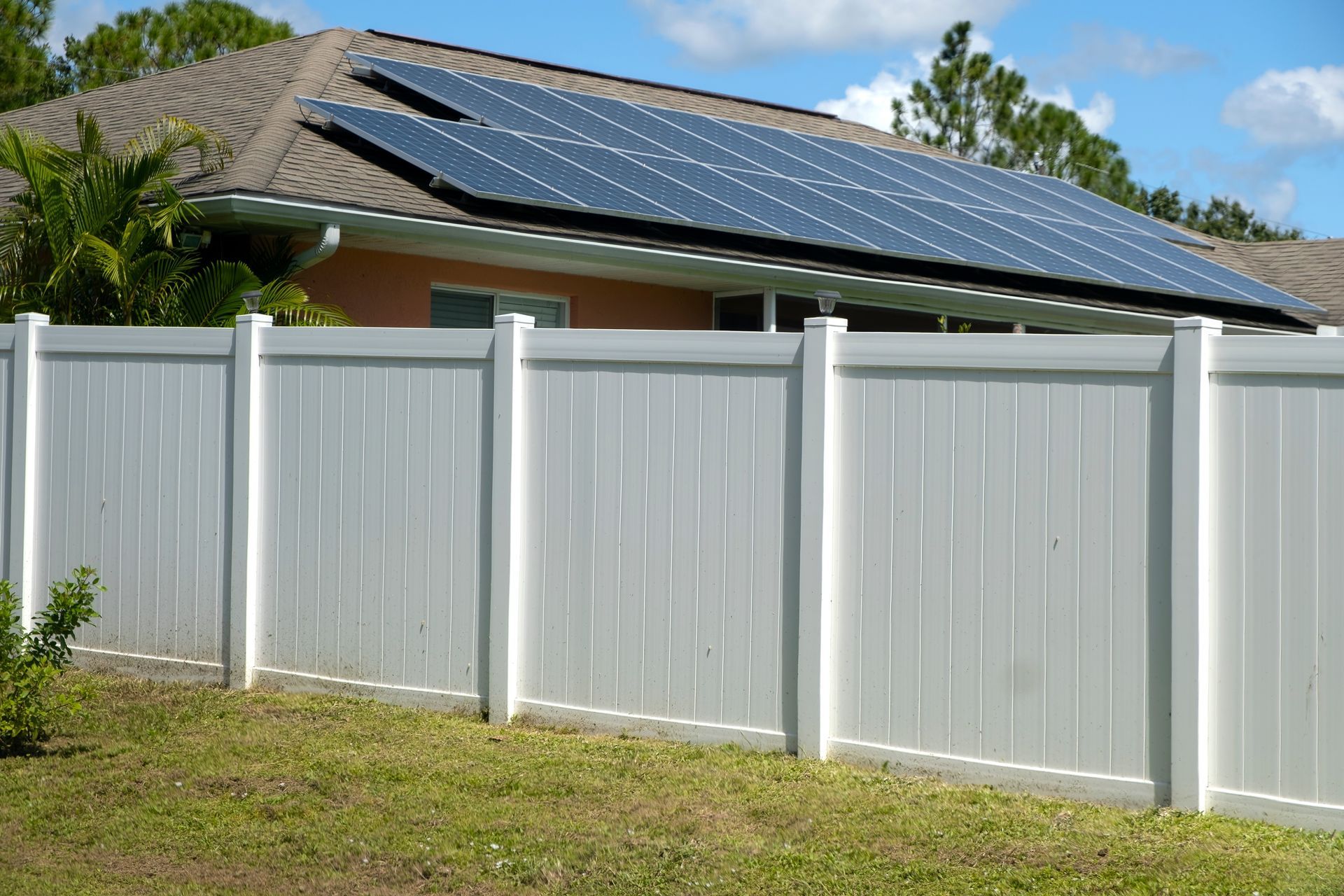 White fence in front of a house with solar panels on the roof.